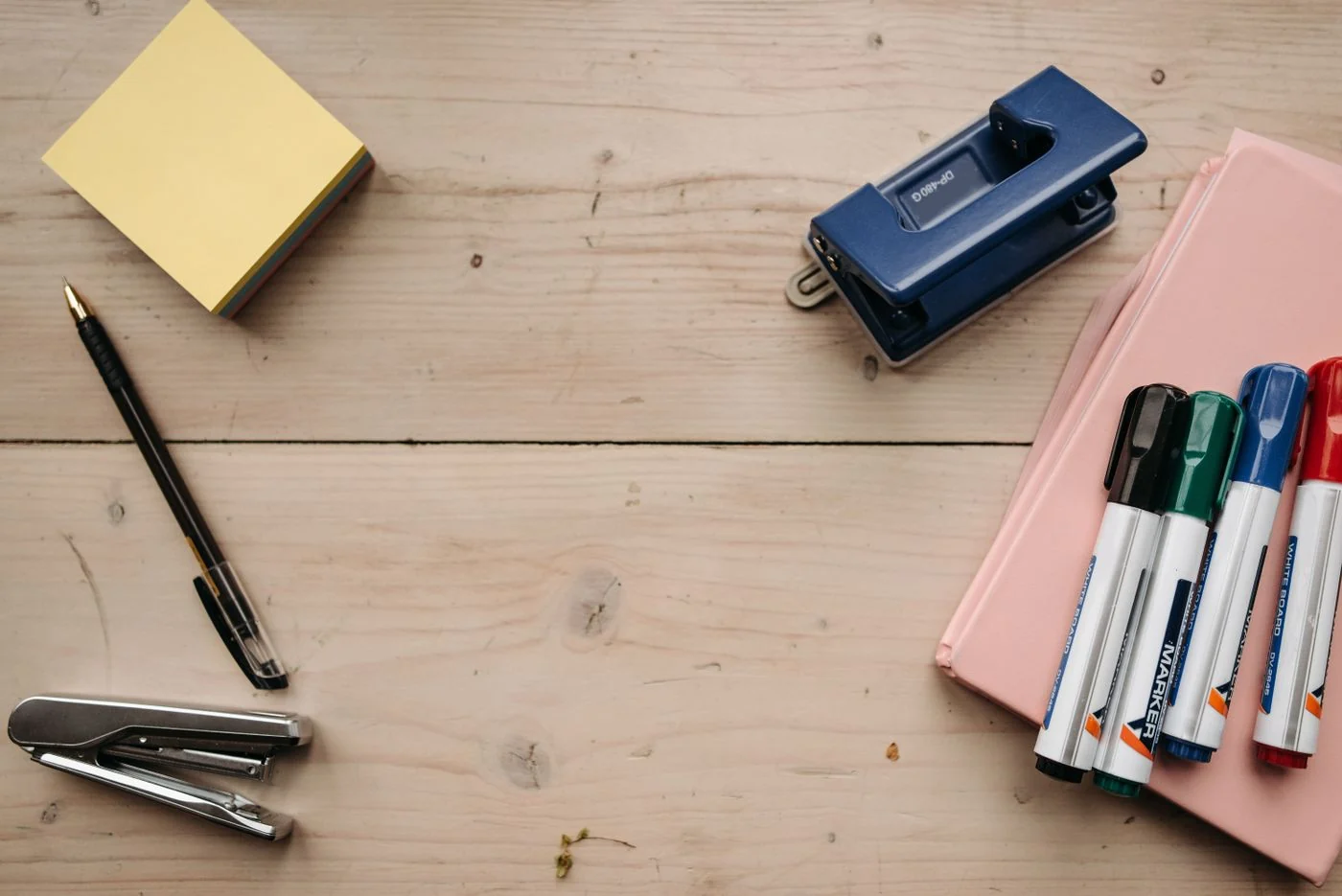 Writing instruments, sticky notes, a stapler and a hole punch on a desk